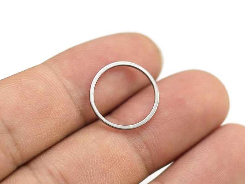 May include: A silver metal ring, approximately 1 inch in diameter, is held between two fingers.