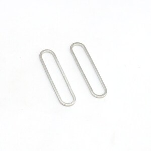 May include: A pair of silver oval-shaped earrings. The earrings are simple and minimalist in design.