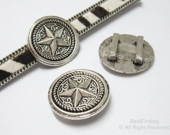 Könnte beinhalten: Silberfarbene Metallknöpfe in Sternform mit dekorativem, seilartigem Rand. Ein Knopf ist an einem schwarz-weiß gemusterten Riemen befestigt. Die Knöpfe haben ein Vintage- oder Antik-Aussehen, geeignet für Bastelarbeiten oder Verzierungen.