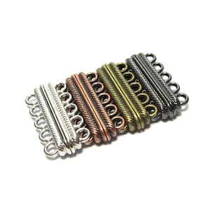 Może przedstawiać: Pięć metalowych zapięć w różnych kolorach do naszyjników lub bransoletek. Zapięcia są srebrne, miedziane, mosiężne, stalowe i czarne.