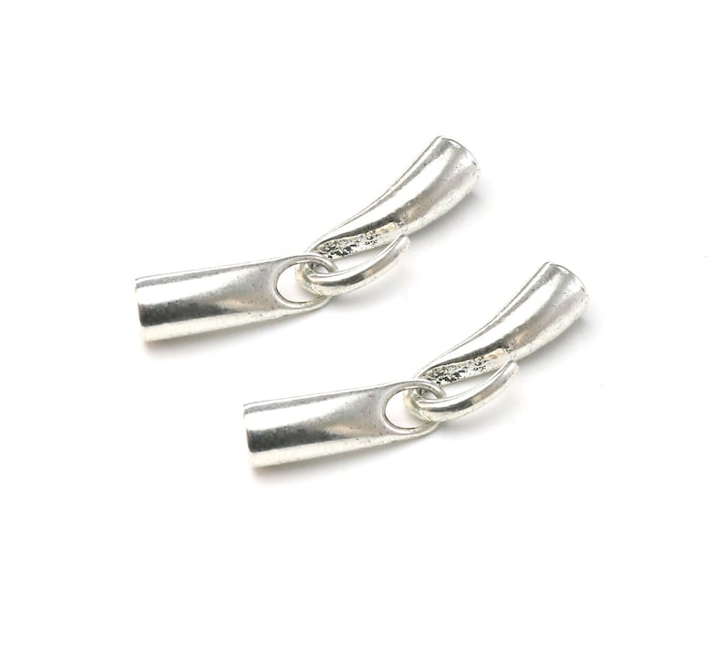 May include: Two silver metal end caps for jewelry making. Each end cap has a curved shape and a small loop for attaching to a chain or cord.