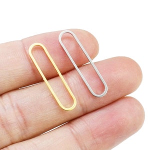 May include: Two oval-shaped metal rings, one gold and one silver, are held in a hand. The rings are about 1 inch long and 1/4 inch wide.