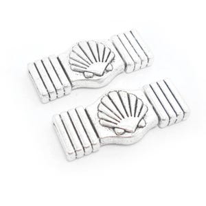 May include: Two silver-toned metal toggle clasps with a raised seashell design. Each clasp has a series of parallel lines on the sides.