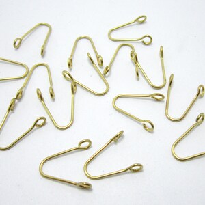 May include: A group of 14 gold-toned metal hooks with a loop at each end. The hooks are arranged in a random pattern on a white surface.