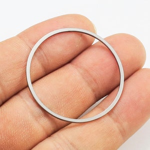 May include: A silver-colored metal ring, held in a hand, with a smooth, polished finish.