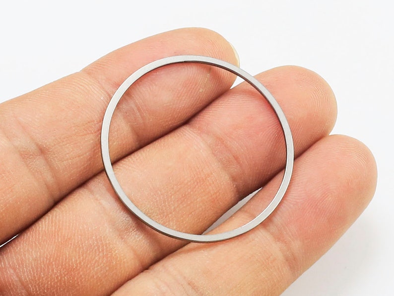 May include: A silver-colored metal ring, held in a hand, with a smooth, polished finish.