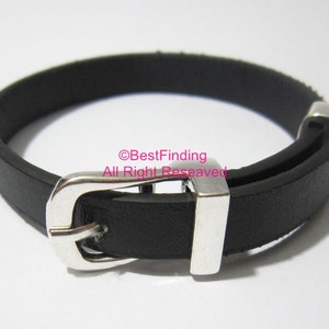 May include: A black leather bracelet with a silver buckle. The bracelet is approximately 2.5 cm wide and has a simple design.