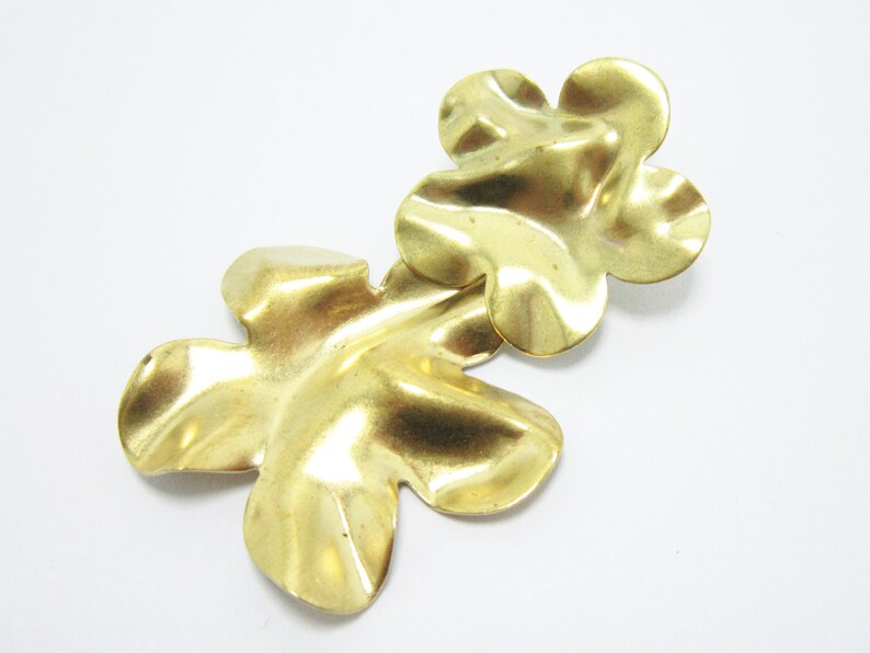 K&ouml;nnte beinhalten: Zwei goldfarbene, metallene Bl&uuml;ten-Anh&auml;nger mit strukturierter Oberfl&auml;che.