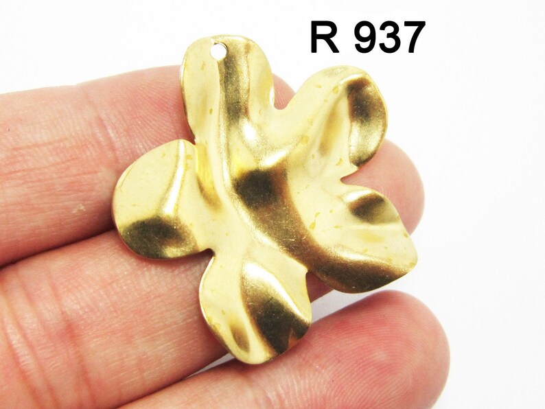K&ouml;nnte beinhalten: Ein goldfarbener Metall-Blumenanh&auml;nger mit strukturierter Oberfl&auml;che. Der Anh&auml;nger hat oben ein Loch zum Anbringen an einer Halskette oder einem Armband.