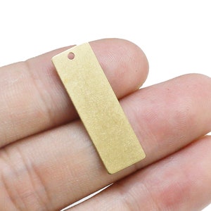 May include: A gold-coloured metal tag with a hole in the centre. The tag is rectangular and has a slightly textured surface.