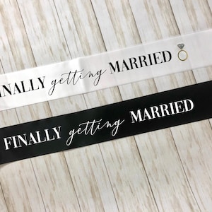 May include: Two white satin sashes with black text. The top sash says "FINALLY getting MARRIED" with a diamond ring icon. The bottom sash says "FINALLY getting MARRIED".