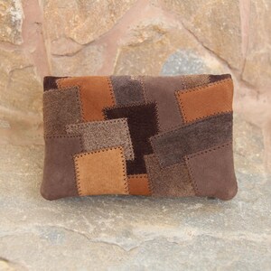 May include: A rectangular clutch bag with a patchwork design in shades of brown. The patches are stitched together, creating a textured surface. The bag is made of suede or a similar material.