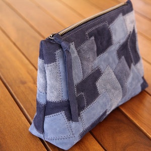 May include: A blue patchwork suede zippered pouch. The pouch is made of different shades of blue suede and has a zipper closure.