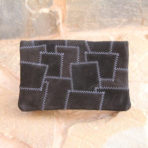 May include: A black suede clutch bag with a patchwork design. The bag is made of different pieces of suede sewn together with white stitching.