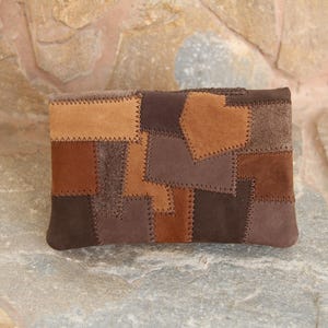 Könnte beinhalten: Eine rechteckige Clutch mit Patchwork-Design. Die Clutch weist verschiedene Brauntöne auf, darunter Beige, Mittelbraun und Dunkelbraun. Die Teile sind mit sichtbaren Nähten zusammengenäht, wodurch eine strukturierte Oberfläche entsteht. Die Gesamtästhetik ist rustikal und handgefertigt.