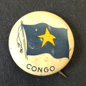 May include: A white button with a blue flag with a yellow star and the word "CONGO" printed on it.