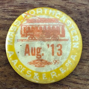 May include: Yellow and orange button with the text "Massachusetts Northeastern A. of S. & E. R. of A." and "Aug. '13" with a picture of a streetcar.