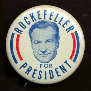 May include: A white button with a blue and red border. The button features a portrait of Nelson Rockefeller and the text "Rockefeller for President".