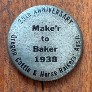 May include: A round, silver-toned pin with the text "25th Anniversary" at the top. The pin reads "Make'r to Baker 1938" in the center, with "Oregon Cattle & Horse Raisers' Ass'n." around the edge. The pin has a pin back.