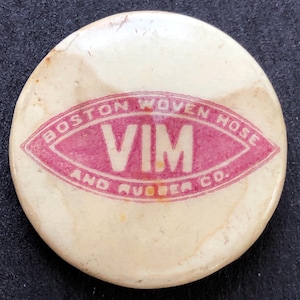 以下が含まれることがあります： ピンクの楕円形のロゴがついた白いボタンで、ロゴには「Boston Woven Hose and Rubber Co.」と書いてあり、楕円形の中に「VIM」という文字がより大きなフォントで書かれています。