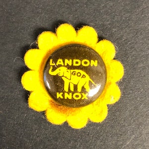 May include: A yellow felt flower pin with a black button featuring a cartoon elephant with the text "LANDON KNOX GOP" in yellow.