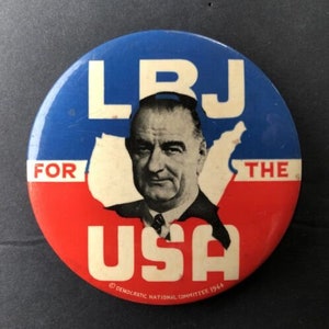 Puede incluir: Un botón de campaña política rojo, blanco y azul con un retrato de Lyndon B. Johnson con el texto "LBJ for the USA" y "Democratic National Committee 1964".