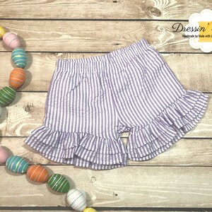 Puede incluir: Shorts de rayas blancas y moradas con un dobladillo con volantes. Los shorts est&aacute;n hechos de una tela ligera y tienen una cintura el&aacute;stica c&oacute;moda.