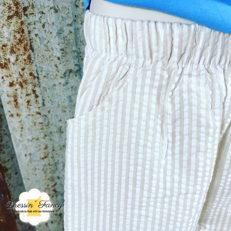 May include: White and beige striped pants with a wide waistband and a pocket on the side. The pants are made of a lightweight fabric and have a relaxed fit.