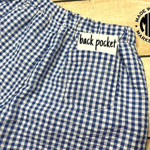 May include: Blue and white gingham shorts with a back pocket and a label that says "back pocket".
