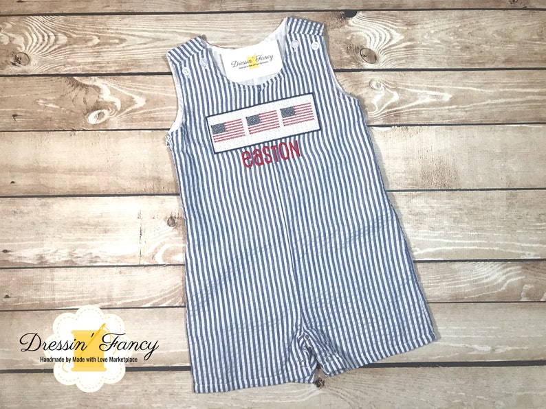 May include: A blue and white striped baby onesie with a red, white, and blue embroidered American flag design and the name "Easton" embroidered below.