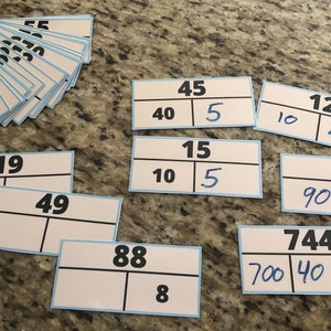 May include: A collection of white flashcards with blue borders and black lines, displaying numbers and equations. The cards feature numbers like 75, 5, 45, 12, 19, 49, 88, 90, and 744, with some cards showing addition problems.