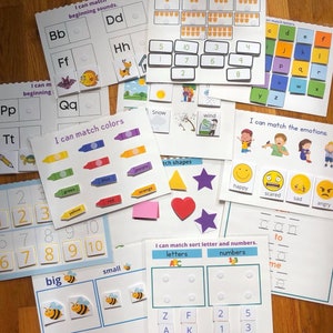 Può includere: Un set di flashcard educative colorate per bambini. Le carte presentano diverse attività, tra cui l'abbinamento di colori, lettere, numeri e forme. Le carte sono stampate su cartoncino bianco e hanno una varietà di illustrazioni e testo.