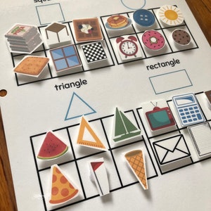 May include: A white worksheet with the title "Sort by Shape" and images of various shapes, including circles, squares, rectangles, and triangles. The images include a pizza, a watermelon, a waffle, a clock, a donut, a sun, a sailboat, a window, a table, a cracker, a cookie, a flag, a ruler, a calculator, a TV, an envelope, a notepad, and a cone.