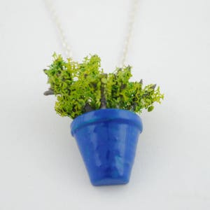 Może przedstawiać: Naszyjnik z niebieskim ceramicznym doniczką i zieloną rośliną.