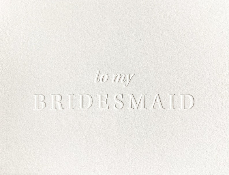 K&ouml;nnte beinhalten: Eine wei&szlig;e Karte mit gepr&auml;gtem Text, der &bdquo;to my BRIDESMAID&ldquo; lautet. Die Karte hat eine strukturierte Oberfl&auml;che und der Text ist in einer einfachen, eleganten Schriftart gehalten. Die &Auml;sthetik ist sauber und minimalistisch.