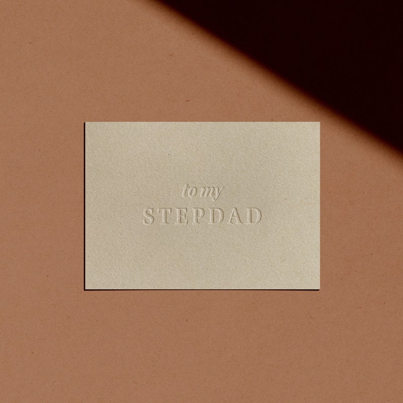 May include: A simple card with the text "to my STEPDAD" embossed in white on a beige background.
