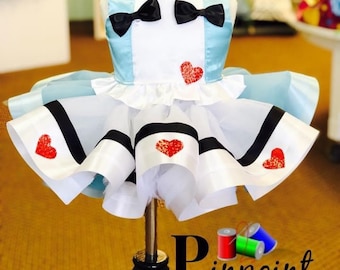 May include: A blue and white dress with a black bow and red heart accents. The dress is on a mannequin and has a white tulle skirt with black and white ribbon trim. The dress is labeled "Pinpoint Designs".