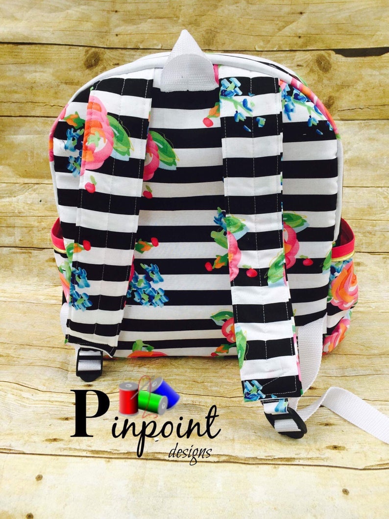May include: Black and white striped backpack with a floral print. The backpack has a white zipper and white straps. The text "Pinpoint Designs" is visible at the bottom of the image.
