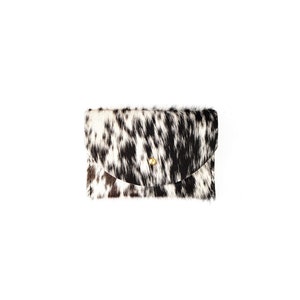 Op de afbeelding: Een clutch met een koeienhuidpatroon in zwart, wit en bruin. De klepsluiting is beveiligd met een goudkleurige knop. De tas is rechthoekig met een gebogen klep.
