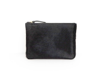 May include: A black leather pouch with a zipper closure. The pouch has a soft, fuzzy texture.