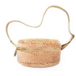 Puede incluir: Un bolso bandolera de piel sintética marrón claro con cremallera dorada y correa de cuero marrón.