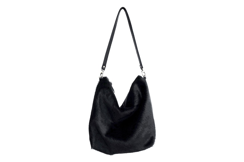 Puede incluir: Un bolso de mano de piel sint&eacute;tica negra con una larga correa de cuero negro.