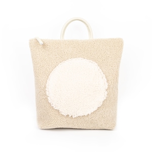 May include: A beige fuzzy tote bag with a large white fuzzy circle on the front.