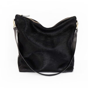 Puede incluir: Un bolso de mano de cuero negro con una correa larga. El bolso tiene una textura suave y peluda.