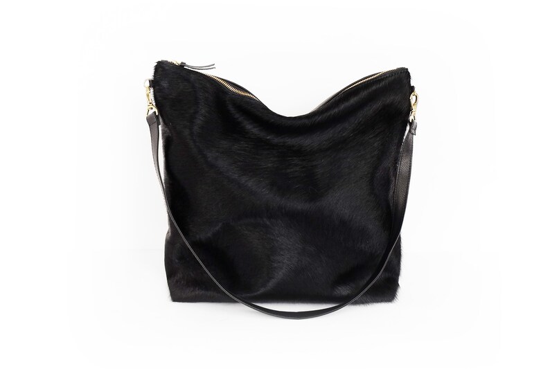 Puede incluir: Un bolso de mano de cuero negro con una correa larga. El bolso tiene una textura suave y peluda.