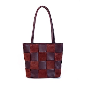 May include: A handcrafted tote bag with a checkerboard pattern. The bag is made of dark brown and burgundy leather squares. It has a matching pair of handles and a rectangular shape.