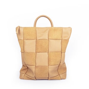 May include: A tan leather tote bag with a woven design. The bag has a single top handle and a zipper closure.