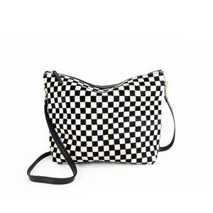Puede incluir: Un bolso bandolera de cuadros blanco y negro con una correa de cuero negra.