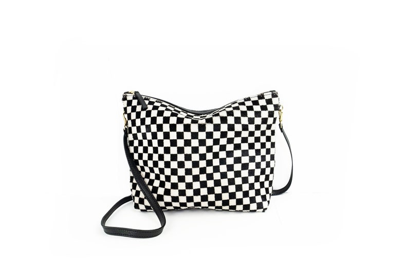 Puede incluir: Un bolso bandolera de cuadros blanco y negro con una correa de cuero negra.