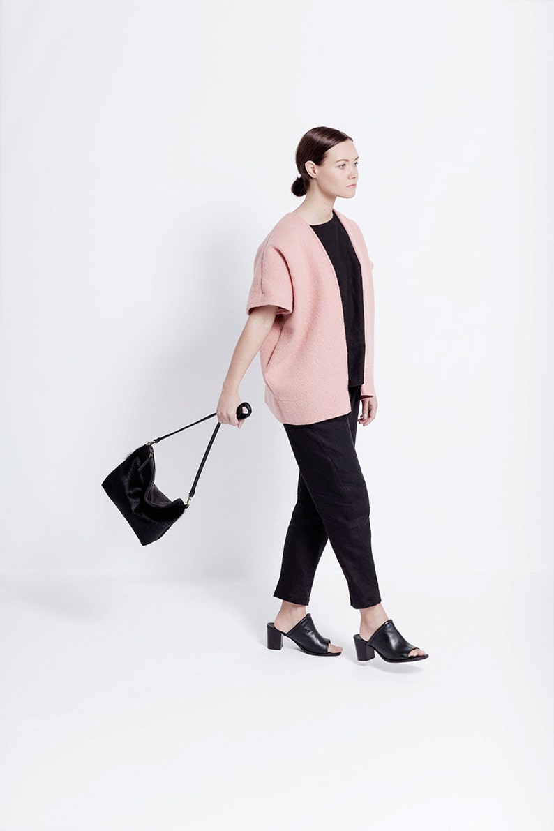 Puede incluir: Una mujer con un c&aacute;rdigan rosa, pantalones negros y mules negras de tac&oacute;n. Lleva un bolso negro con una correa larga.